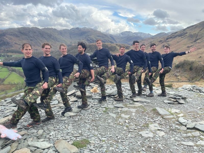 Group of men standing in a line with their left legs raised, on top of a Lake District mountain
