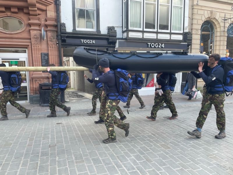 Group of people dressed in camo and carrying a boat through Keswick town centre
