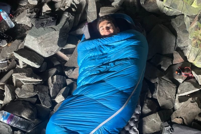 Man lying in a blue sleeping bag on rocks in a cave