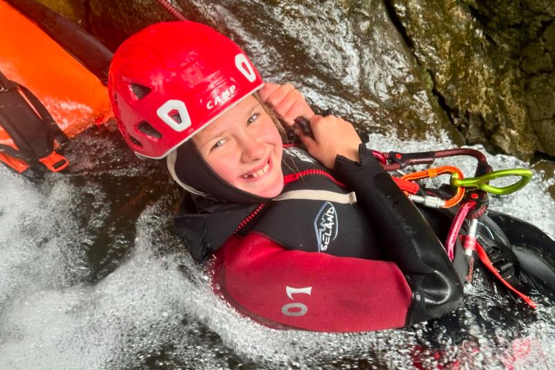 Child sitting on top of a waterfall during ghyll scrambling
