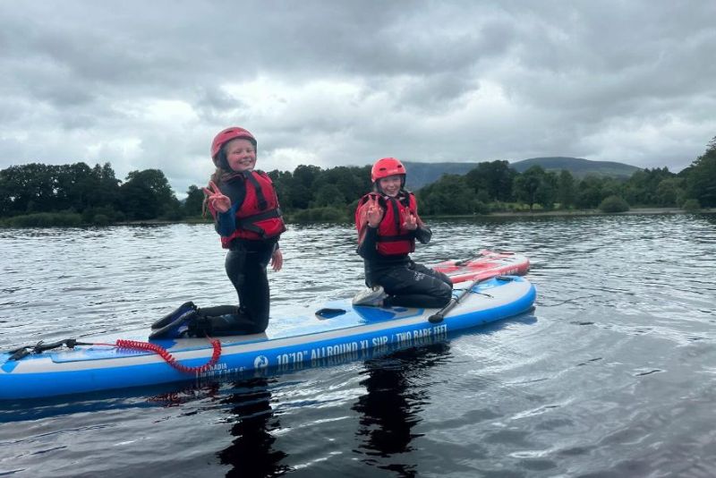 Two girls smiling on a paddle board on Derwentwater