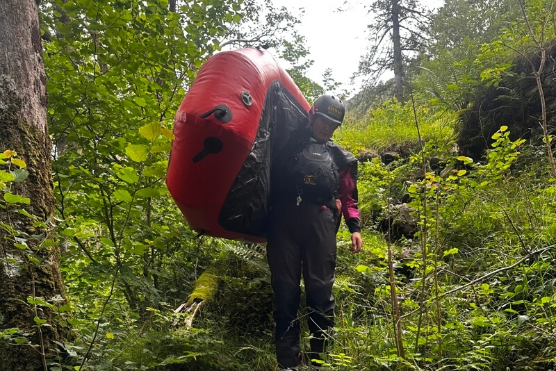 Person carrying a packraft through woodland