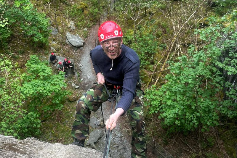 Man looking back up as he abseils down a cliff face