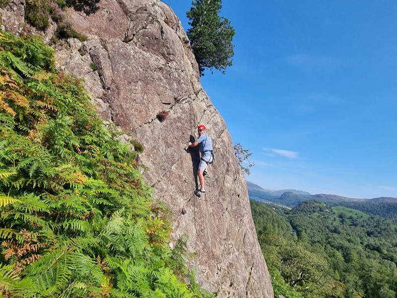 Man climbing a rock face with Lake District mountains in the background