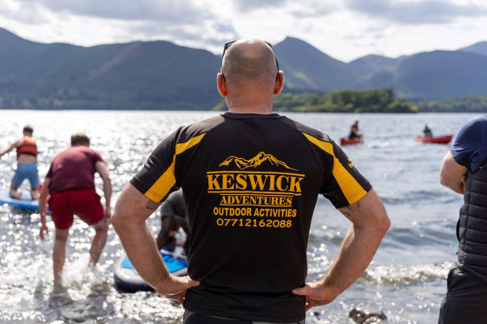 Lee Simpson in a Keswick Adventures t-shirt standing in front of Derwentwater