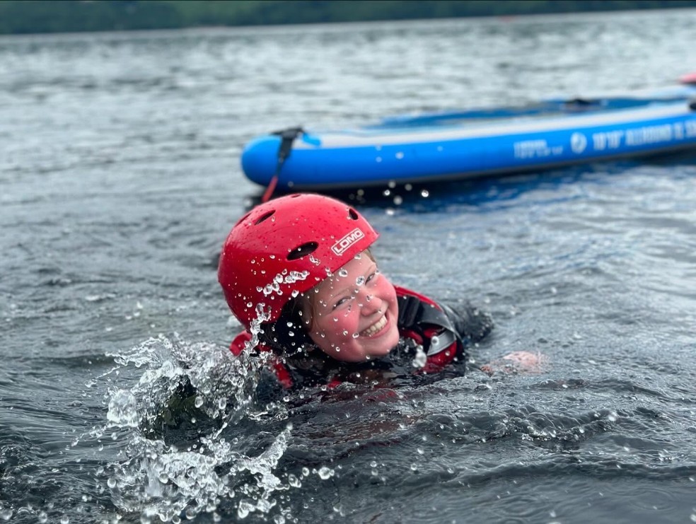 Child swimming and smiling in Derwentwater with a paddleboard in the background